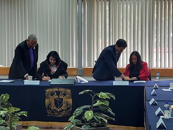 Foto 1- Araceli Romo Cabrera y Gladys Díaz firman el Convenio ULAC - UNAM. El mantel azul oscuro que cubre la mesa lleva el logotipo de la UNAM.